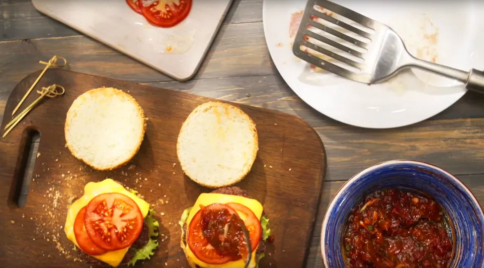 На нижню частину булки викладіть котлетки, потім помідор, соус, і накрийте верхньою частиною.